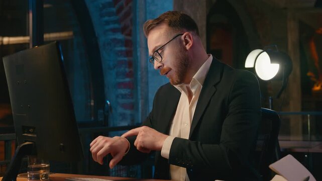 Caucasian fatigued boring stressed business man with computer checking time looking at wristwatch tired executive businessman male professional overworked job at night evening office deadline suffer