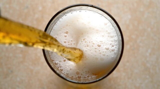 Top down view of beer being poured into glass forming thick white foam and bubbles representing drink service