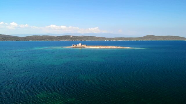 Aerial view of a small island with an old castle ruin surrounded by turquoise water and distant hills, Cunda Island, Ayvalik, Balikesir, Turkey.