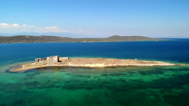 Aerial view of an island with old ruins surrounded by vibrant turquoise and deep blue waters under a clear sky, Cunda Island, Ayvalik, Balikesir, Turkey.
