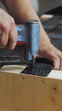 Vertical video. Worker making sofa at furniture factory, close-up of hands. Worker working with pneumatic gun, slow motion.