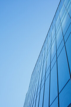 Reflective business office building facade made of glass and clear blue sky. Minimalistic abstract geometric pattern.Contemporary background, modern exterior, urban architecture.