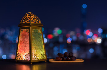 Lantern and small plate of dates fruit with night sky and city bokeh light background for the Muslim feast of the holy month of Ramadan Kareem.