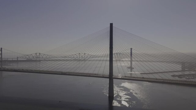 Aerial view of the iconic Forth Bridges spanning the calm waters, creating a striking contrast against the muted sky, South Queensferry, United Kingdom.