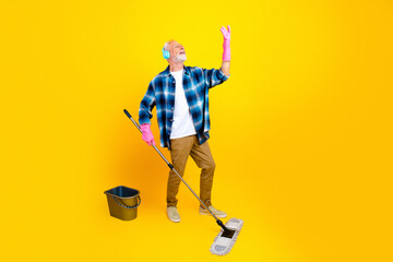 Senior man happily mopping floor with headphones and pink rubber gloves against bright yellow...