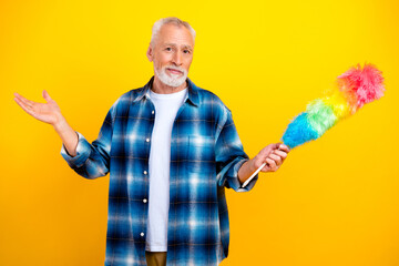 Senior man holding a colorful feather duster and shrugging with a playful, reluctant attitude...