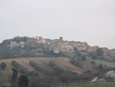 Borgo collinare con case storiche, raccolte attorno a una torre centrale. Il paese domina il paesaggio rurale circostante, con campi terrazzati e vegetazione sparsa 