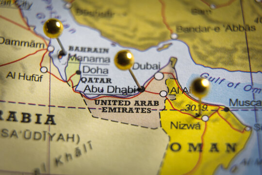 Close-up of a geographical map of the United Arab Emirates and Gulf region with gold push pins marking major cities like Abu Dhabi, Dubai, and Muscat