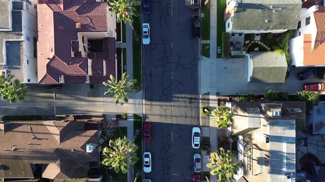 Straight residential corridor near Coronado Ave, Bluff Park shows cracked asphalt, parked cars, palm lined sidewalks in tight coastal grid. Tile roofs, long shadows, warm light, Long Beach, CA