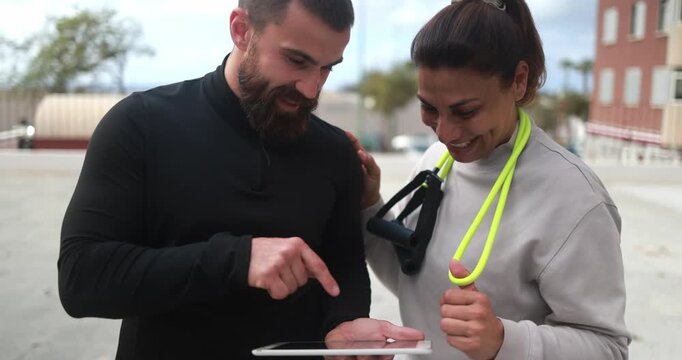 Happy latin woman and her personal trainer checking workout plan on tablet outdoor - Sport, healthy lifestyle and fitness concept