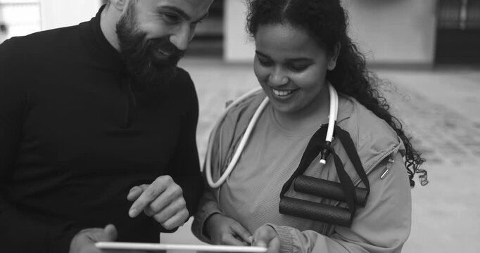 Personal trainer explaining workout plan to curvy latin girl on tablet - People, outdoor sport and diet concept - Black and white editing