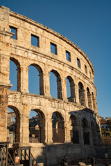 Obraz premium Epic Pula arena ancient Roman architecture vertical panorama. Cinematic low angle view of historic monument amphitheater ruins, limestone columns, arcade arches and golden sunset sky. 