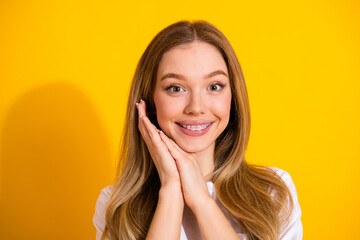 Bright smiling young woman with braces posing with hands on cheeks against a vibrant yellow...