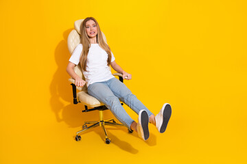 Young woman in casual white shirt sits in an office chair against a bright yellow background...