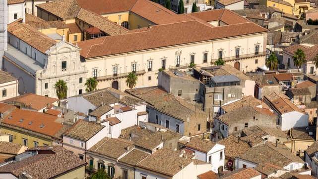 Aerial view of the Cathedral of Melfi, Basilicata, Italy. It's a historic church featuring a long white facade with numerous windows, nestled within the dense urban neighborhood. Sunny morning.