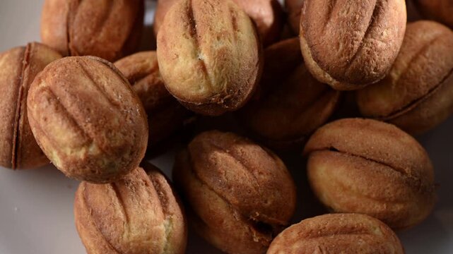 Close up of nut-shaped cookies filled with creamy condensed milk, slowly rotating on a turntable. Golden-brown shells, textured surface, and smooth filling captured in high detail. Sweet bakery treat,