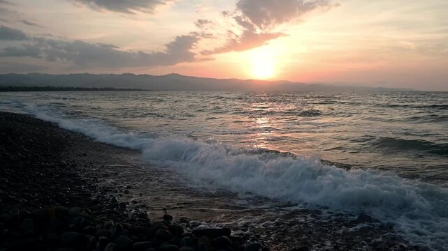 Beautiful sunset on the coast of Cyprus with warm orange and pink hues reflecting on the calm Mediterranean Sea. Silhouetted shoreline, gentle waves, and soft clouds create a serene and romantic atmos