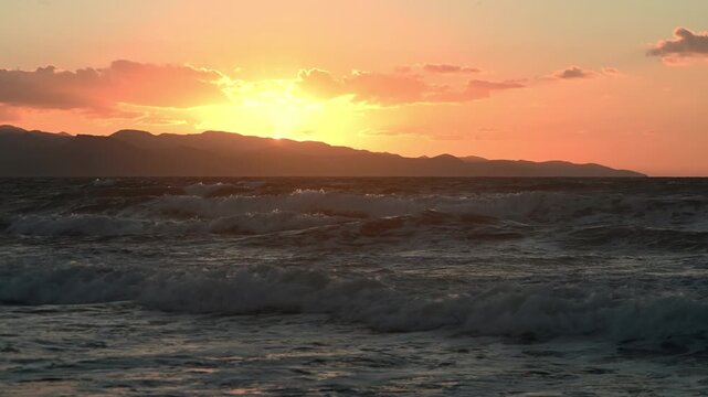 Scenic view of a stunning sunset over the coastline of Cyprus, with golden and pink hues reflecting on the calm Mediterranean Sea. Silhouetted rocks and gentle waves create a serene, peaceful, and rom