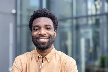 Fototapeta premium Young businessman with afro hairstyle smiling confidently outdoors in an urban setting, smart-casual and approachable, portrait conveying success, leadership and a bright future