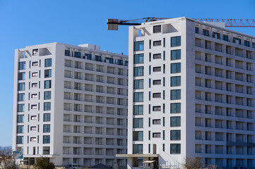 Fototapeta premium Modern residential buildings under construction with a crane against a clear blue sky
