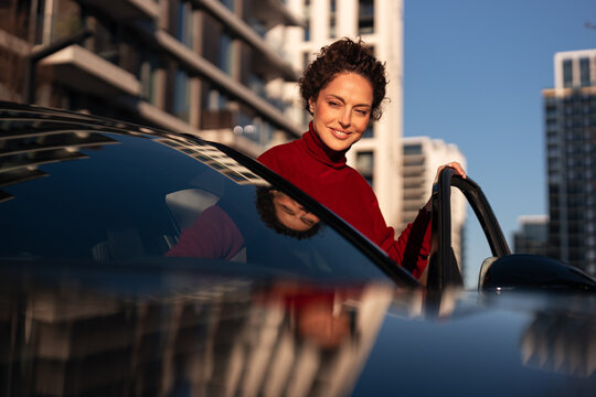 Woman smiling opening car door in city setting