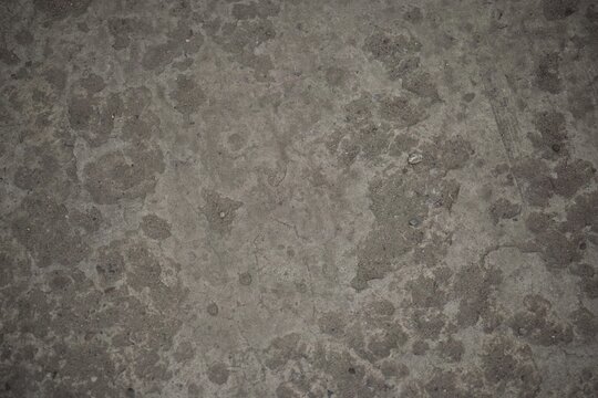 Textured weathered gray concrete surface with dark patches and a grainy finish.