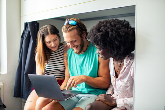 Three friends using a laptop in a hostel bunk