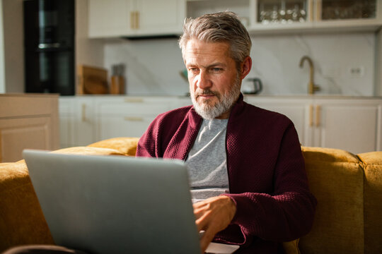 Mature man working on laptop in home kitchen