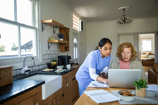 Nurse assisting elderly woman with laptop at home kitchen