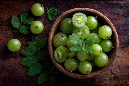 Overhead shot of gooseberries in a wooden bowl with leaves on wood