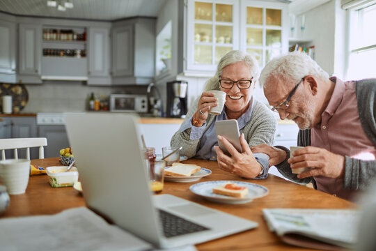 Smiling senior couple using smartphone at breakfast in home kitchen
