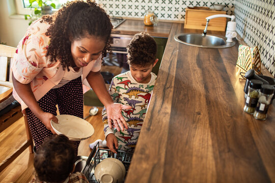 Mother teaching children to load the dishwasher in a home kitchen