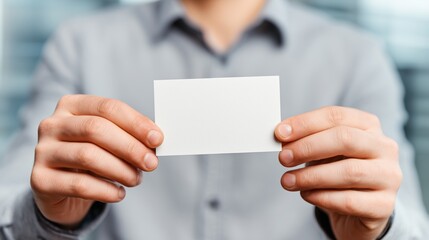 Person holding a blank card in both hands while sitting indoors with a soft background and focused expression on a clear day
