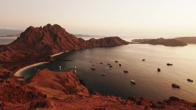 Majestic aerial view of Padar Island in Komodo National Park, showing the iconic rugged hills and picturesque bay filled with tour boats during a spectacular golden sunrise in Indonesia