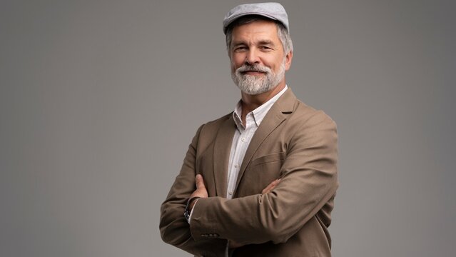 Attractive serious grey-haired man in suit and flat cap isolated on grey