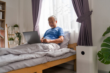 Fototapeta premium Elderly retired male using laptop computer online or surfing internet in bed at home