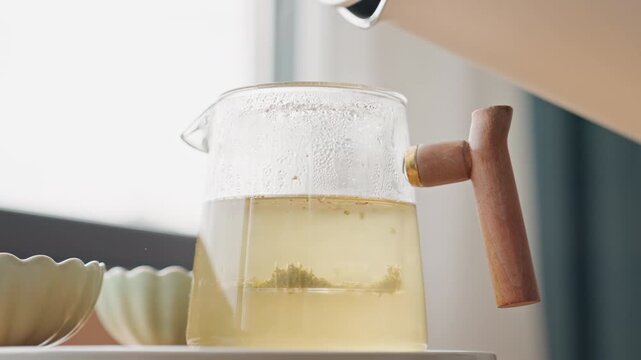 Hotel kettle pouring water into teapot, clear glass carafe on tray, steam rise, brewing ritual captured in natural light, breakfast preparation, barista pouring, minimal modern suite
