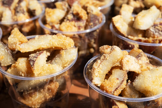 Close-up shows crispy golden fried pork cracklings, or Torresmos, in plastic cups. 