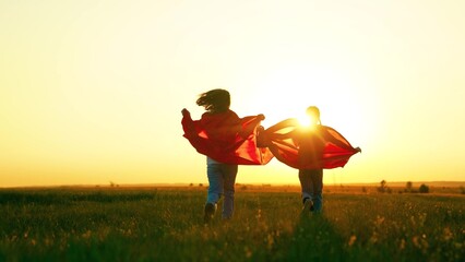 Kids girls play superheroes in red capes in park on green grass, dream. Children in red capes run...