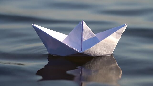 White origami paper boat floating on calm rippling water at sunset