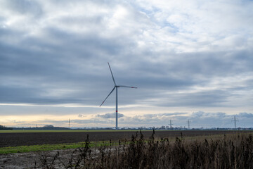 Obraz premium A wind turbine is in the middle of a field with a cloudy sky