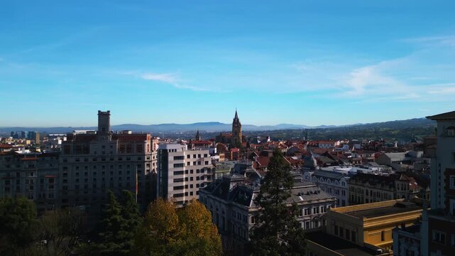 Cinematic 4K aerial vertical rise from trees with tilt-down to Oviedo city. Autumn park and historic architecture in Asturias, Spain.
