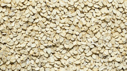 Dense top down view shows large quantity of light colored  flattened grains or seeds such as rolled oats spread across the entire frame