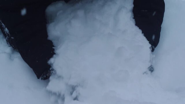 A child in winter clothes scoops up a large armful of fluffy fresh snow. A close-up of winter fun and outdoor activities on a frosty day.