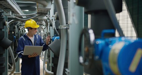 Professional industrial technician is inspecting pipeline valves with a laptop in a modern...