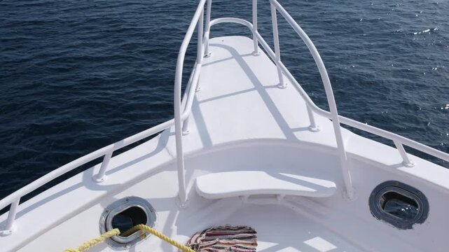 Boat deck displays colorful blanket and mooring rope, leading to a clear view of calm ocean water and railing structure in the background