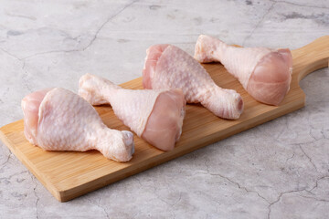 Fresh chicken drumsticks arranged on a wooden cutting board ready for cooking in a kitchen setting