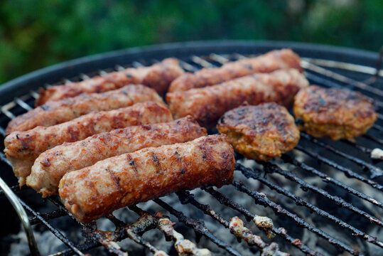 Close-up of sausages and meatballs cooked on a charcoal grill. Outdoor barbecue scene with smoke, rustic cooking and traditional grilling, perfect for summer gatherings and culinary concepts.