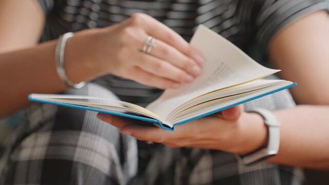 Woman reading peacefully. Guest flips pages in hotel room. Woman gently flipping through book beside warm window light. Calm guest softly turning pages while enjoying peaceful hotel reading session