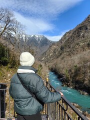 A woman stands with her back to the blue mountain river of Abkhazia.